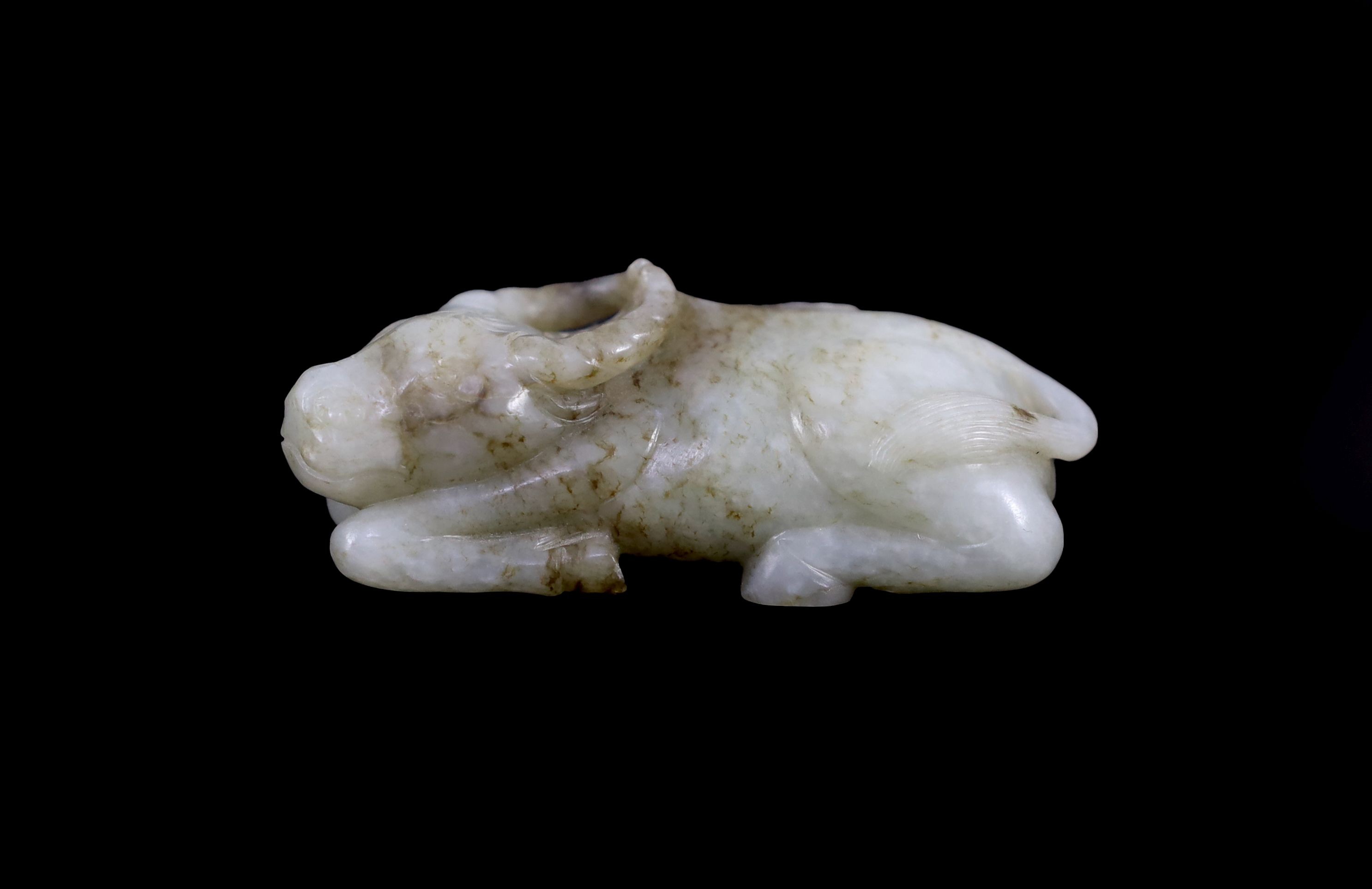 A Chinese Ming pale celadon and brown jade figure of a recumbent Buffalo, 16th/17th century, 8cm long
